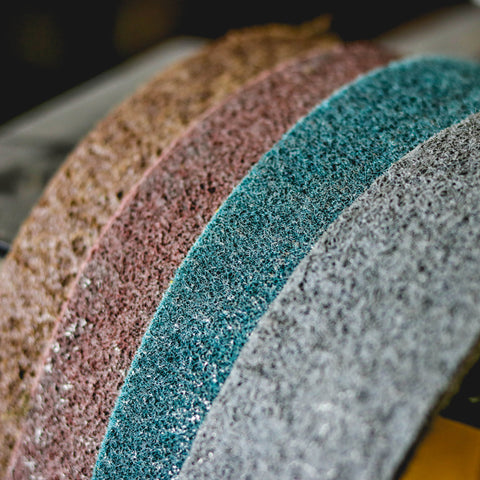 Pack of four 2-1/2 x 60 non-woven surface conditioning belts in brown, maroon, blue, and grey for various grit finishes.